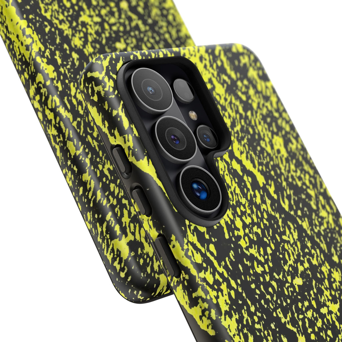 A close-up of a smartphone case with a black and neon yellow splatter pattern, fitted on a phone with a triple-camera system, shown against a plain white background.