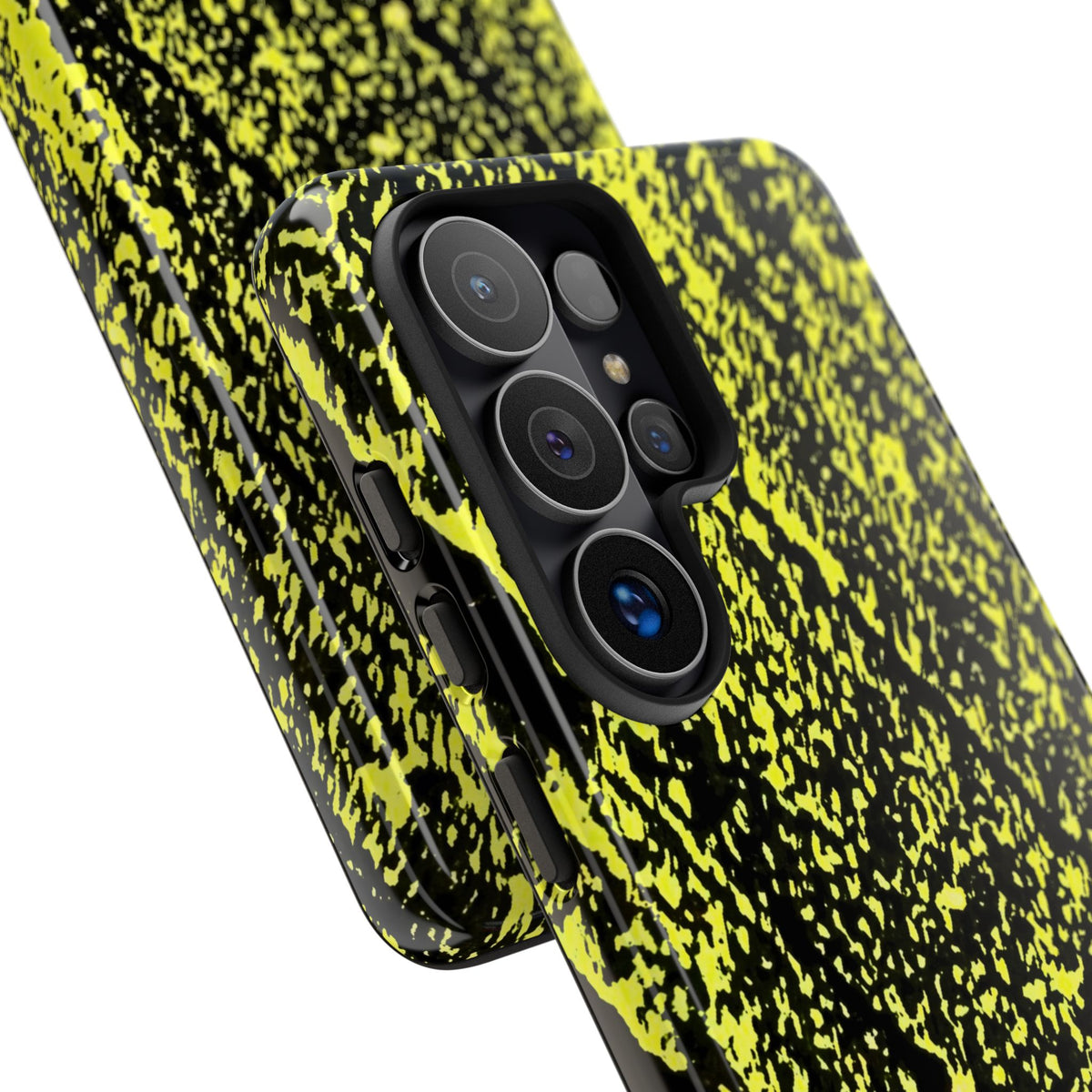 A close-up of a smartphone case with a black and neon yellow splatter pattern, shown fitted on a phone against a plain white background.