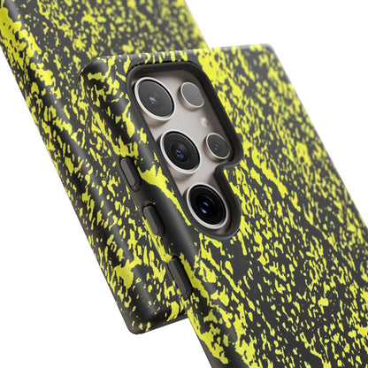 A close-up of a smartphone case with a black and neon yellow splatter pattern, fitted on a phone. The case features a raised camera bumper and side button covers, shown against a clean white background.
