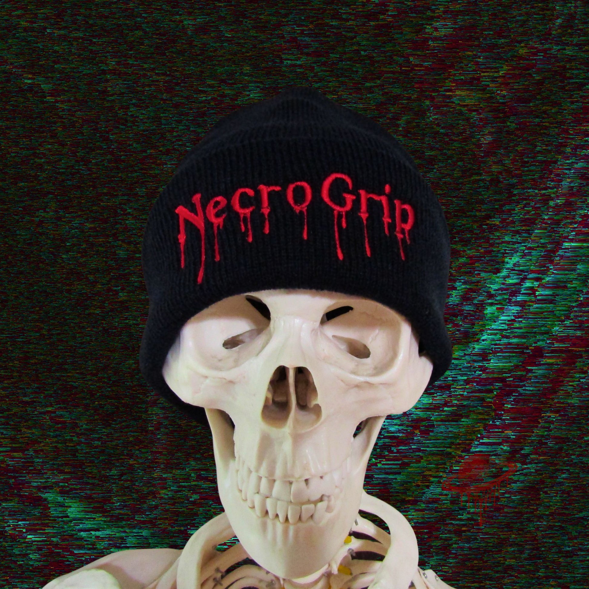 Skeleton model wearing black cuffed beanie embroidered with NecroGrip drip logo in blood-red thread, glitch-distorted background.